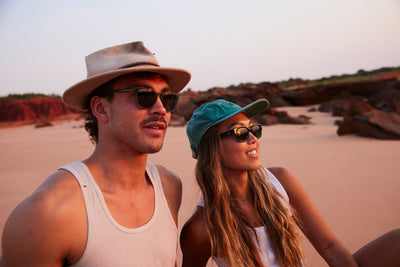 man and woman watching sunset wearing sunglasses and hats